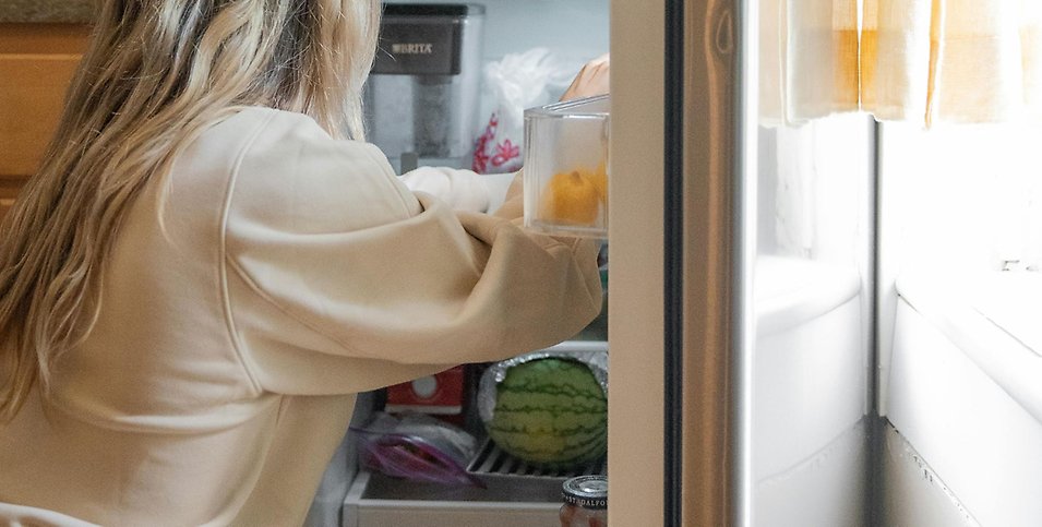 En kvinna plockar in i ett kylskåp.